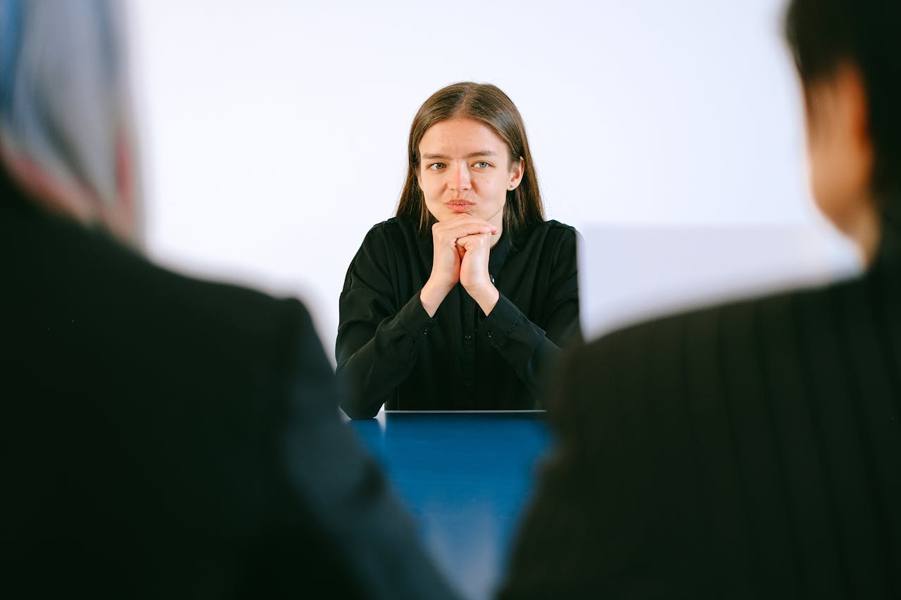 Services A woman in a job interview facing two people at an office table, focusing intently.