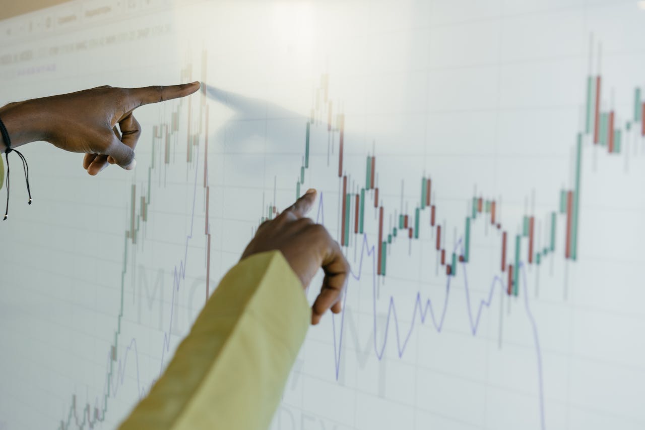 Hands pointing at a financial stock chart on a digital screen, highlighting data analysis and trends.